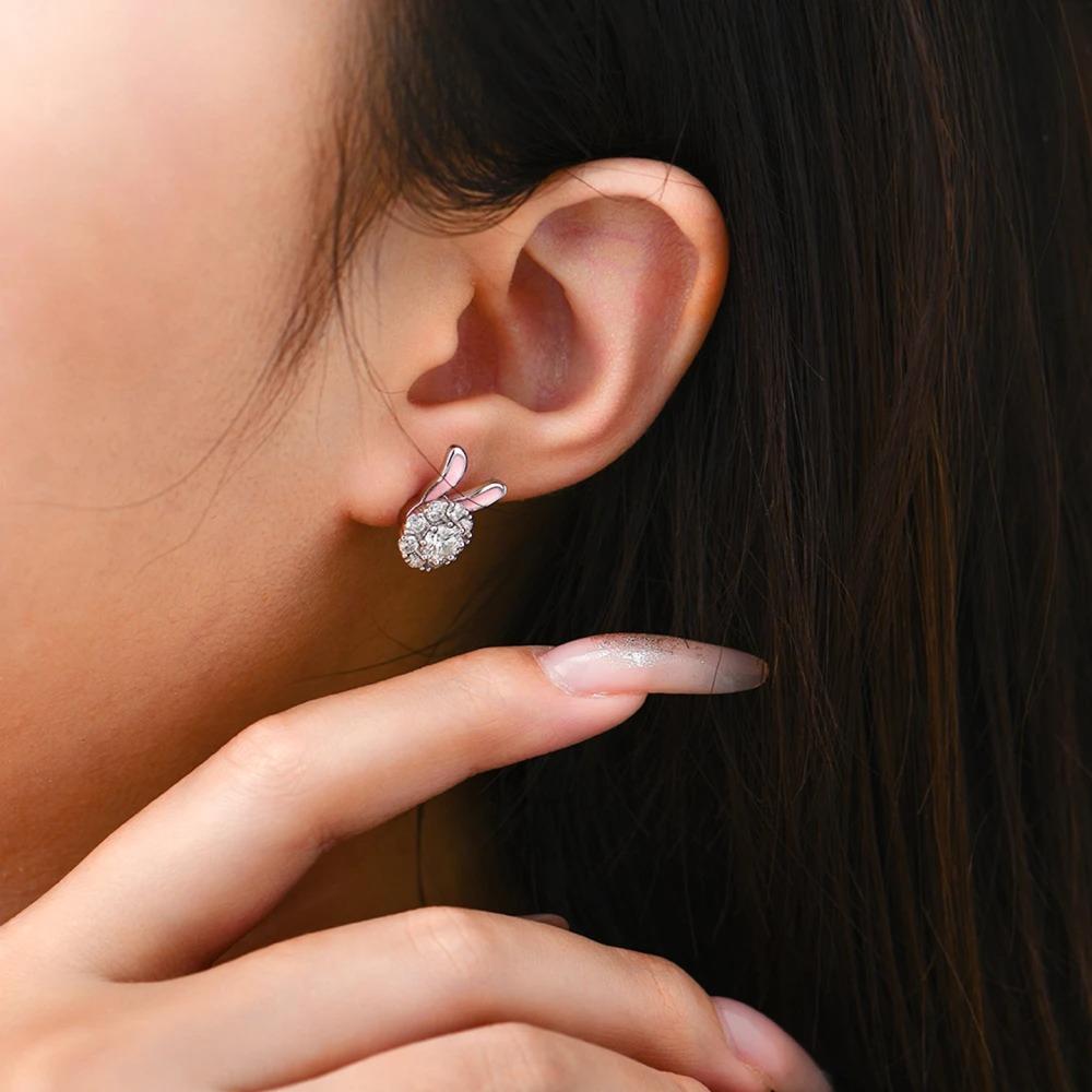Close-up of an ear wearing a diamond earring with a hand adjusting it.