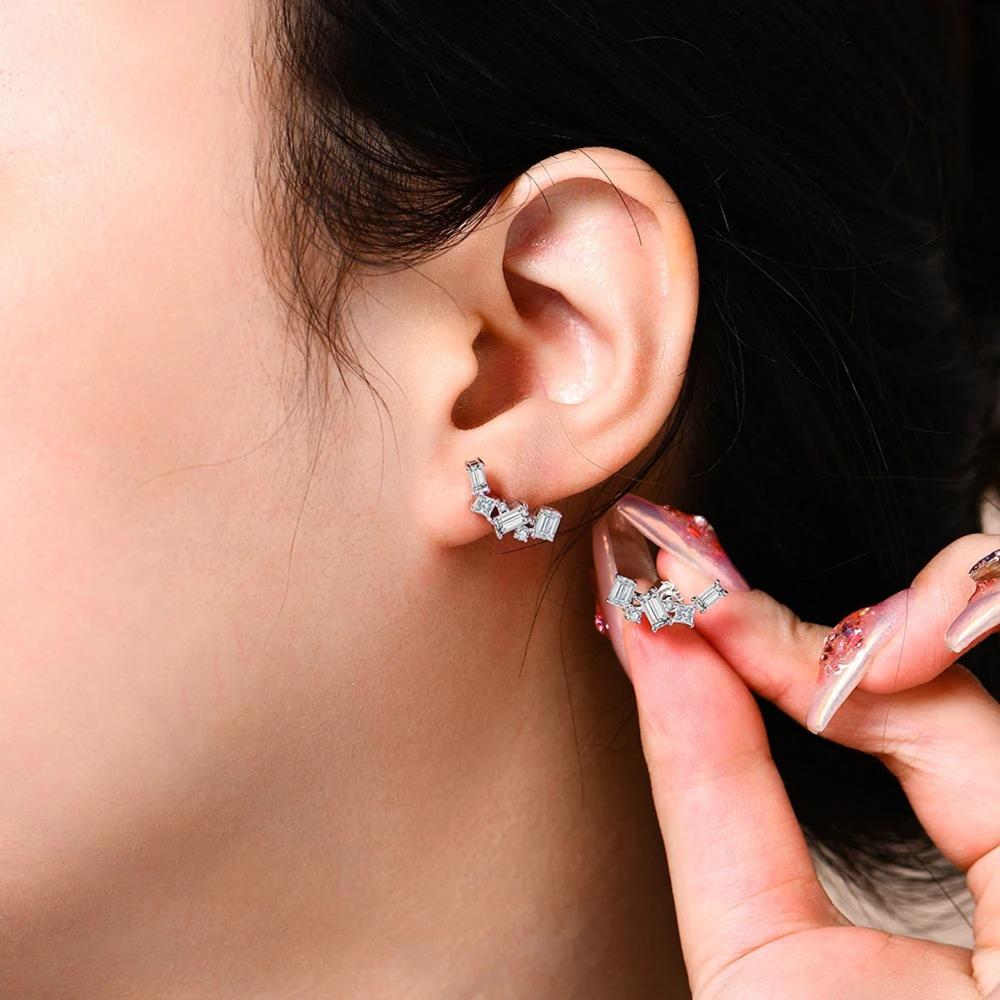 Close-up of an ear wearing a silver earring with a hand holding another earring.