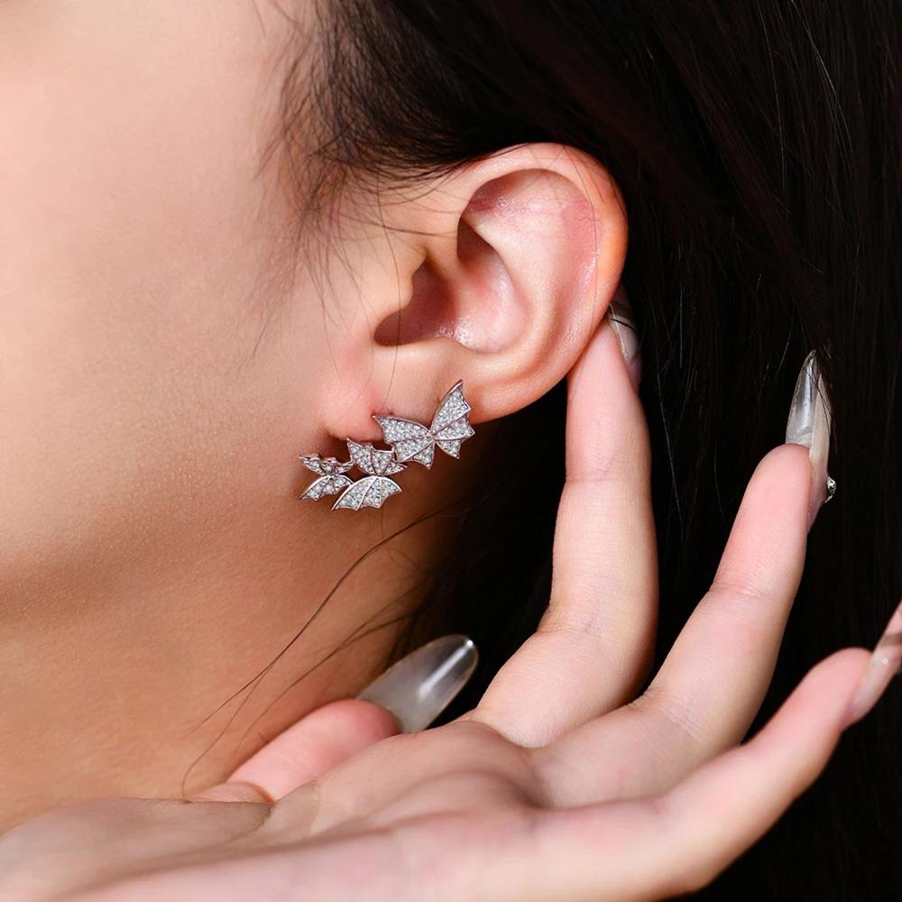 Close-up of a person wearing butterfly-shaped earrings with a hand adjusting them.